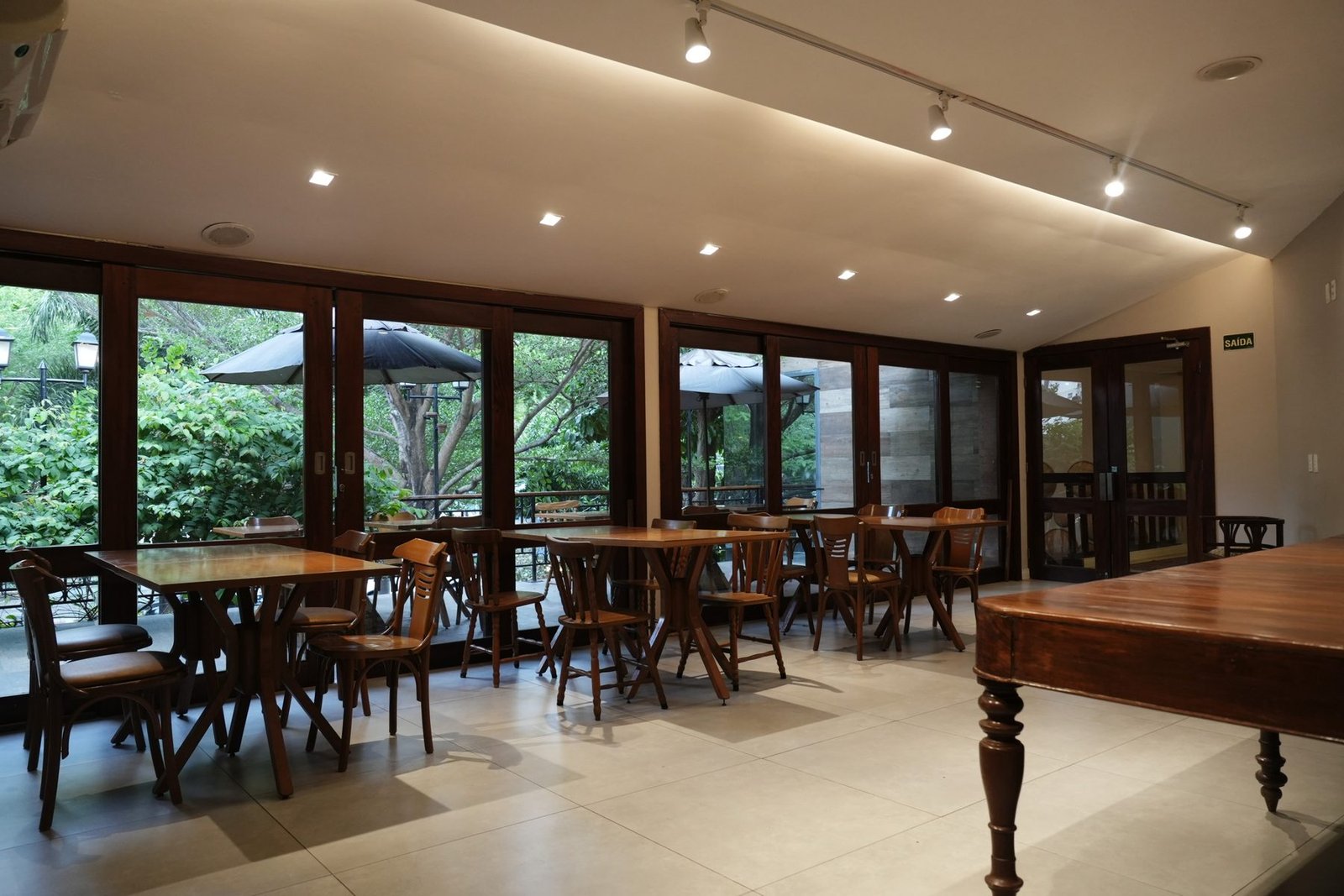 Salão do Terrazo montado para evento corporativo em Fortaleza, com mesas de madeira e janelas amplas para a varanda arborizada